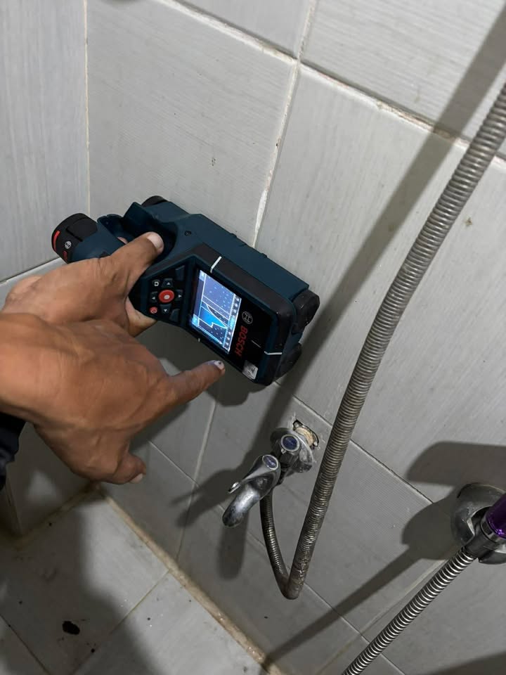 Tubero Specialists technician using an advanced water leak detection scanner against a tiled bathroom wall
